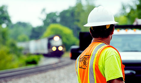 A worker in a safety vest watches a train approaching.